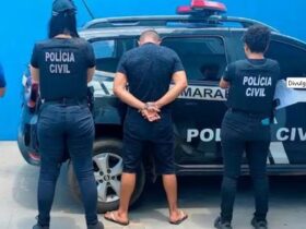 Foto de policiais em frente à uma viatura da Policia Civil com um homem preso por ter fotos e vídeos pornográficos infantis do próprio filho adotivo e de outras crianças.
