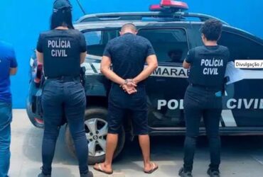 Foto de policiais em frente à uma viatura da Policia Civil com um homem preso por ter fotos e vídeos pornográficos infantis do próprio filho adotivo e de outras crianças.