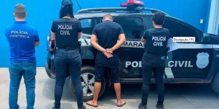 Foto de policiais em frente à uma viatura da Policia Civil com um homem preso por ter fotos e vídeos pornográficos infantis do próprio filho adotivo e de outras crianças.