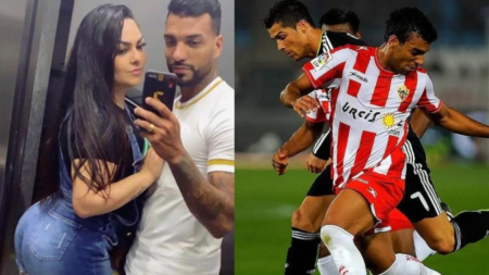 Jogador de futebol com uma camisa branca, um celular na mão acompanhado de sua esposa, de cabelos longos e blusa presa.