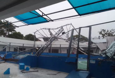 Espaço dentro de uma escola de cor predominantemente azul com uma quadra de esportes sem a cobertura