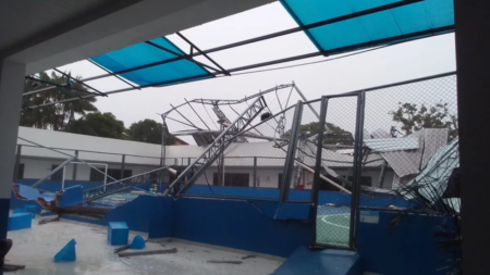 Espaço dentro de uma escola de cor predominantemente azul com uma quadra de esportes sem a cobertura