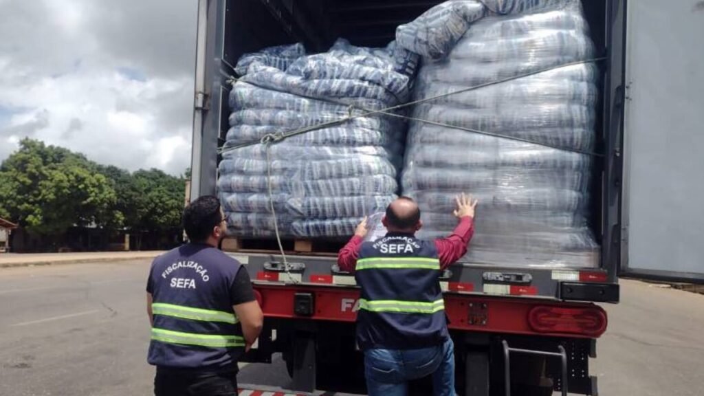 Caminhão cheia visto de trás com dois grandes sacos de mercadoria e duas pessoas de roupa cinza