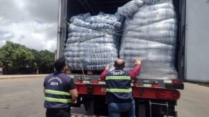Caminhão cheia visto de trás com dois grandes sacos de mercadoria e duas pessoas de roupa cinza