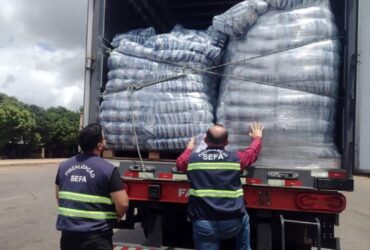 Caminhão cheia visto de trás com dois grandes sacos de mercadoria e duas pessoas de roupa cinza