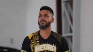 Homem com um chapéu de palha e camiseta branca. Ele segura um microfone