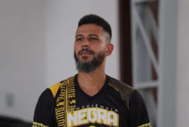 Homem com um chapéu de palha e camiseta branca. Ele segura um microfone
