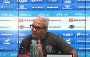 Senhor de meia idade, de blusa preta, de óculos falando diante de um microfone
