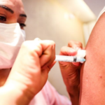 Mulher de máscara descartável aplicando vacina no braço de uma pessoa