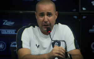 Treinador de futebol careca dando uma entrevista coletiva