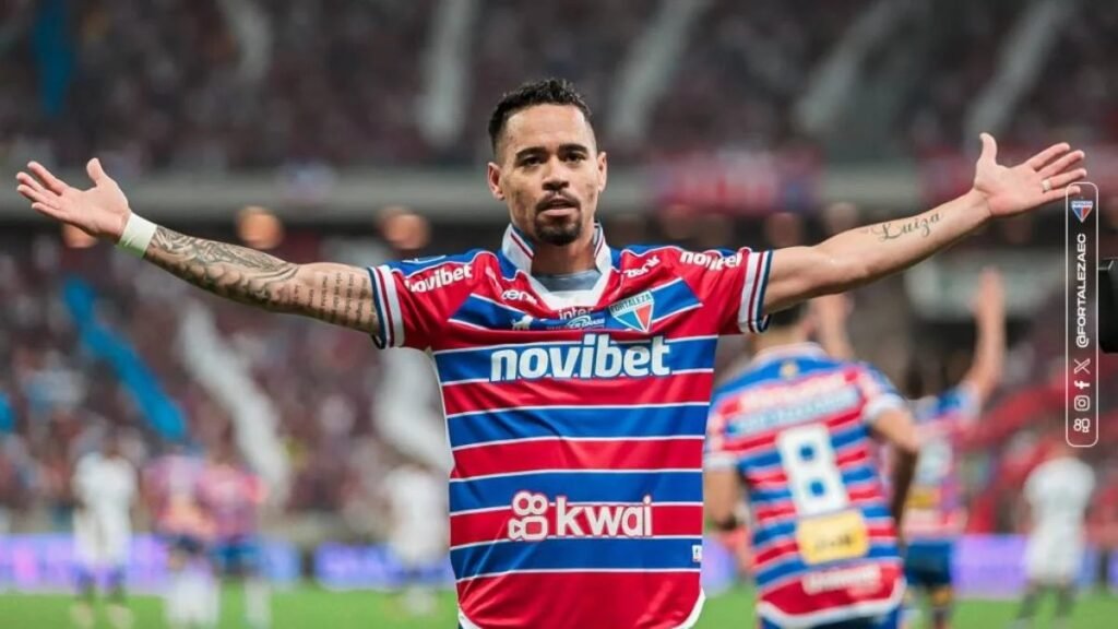 Jogador de futebol de braços abertos comemorando um gol