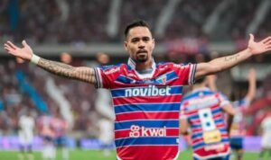 Jogador de futebol de braços abertos comemorando um gol