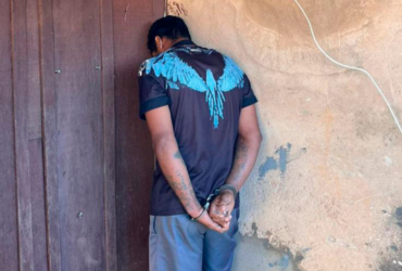Homem de camisa preta com detalhes azuis algemado de frente para uma parede.