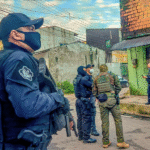 Policiais armados participam de operação em área urbana de Belém (PA), durante ação integrada de combate a facções criminosas. Na imagem, agentes da Polícia Civil e unidades táticas conversam diante de uma residência enquanto monitoram o entorno de uma rua residencial.