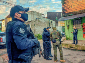 Policiais armados participam de operação em área urbana de Belém (PA), durante ação integrada de combate a facções criminosas. Na imagem, agentes da Polícia Civil e unidades táticas conversam diante de uma residência enquanto monitoram o entorno de uma rua residencial.