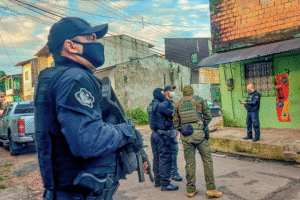 Policiais armados participam de operação em área urbana de Belém (PA), durante ação integrada de combate a facções criminosas. Na imagem, agentes da Polícia Civil e unidades táticas conversam diante de uma residência enquanto monitoram o entorno de uma rua residencial.