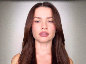 Imagem mostra uma mulher jovem olhando diretamente para a câmera, com expressão séria e neutra. Ela está em fundo claro e aparece do peito para cima.