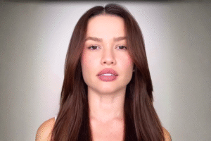 Imagem mostra uma mulher jovem olhando diretamente para a câmera, com expressão séria e neutra. Ela está em fundo claro e aparece do peito para cima.