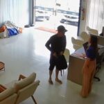 homem vestido de preto, com boné, em pé abordando vítima durante assalto em loja