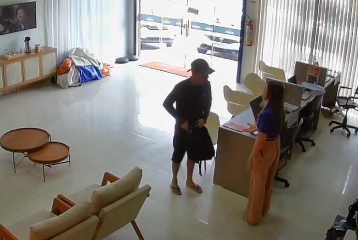 homem vestido de preto, com boné, em pé abordando vítima durante assalto em loja