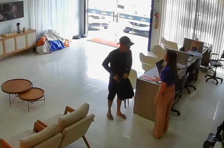 homem vestido de preto, com boné, em pé abordando vítima durante assalto em loja