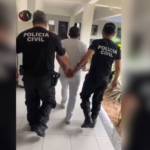 Dois agentes da polícia conduzem um homem detido, segurando-o pelos braços.