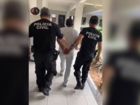 Dois agentes da polícia conduzem um homem detido, segurando-o pelos braços.