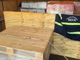 Apresentação da carda de uísque apreendida. As garrafas estão dentro de caixotes de madeiras, por cima deles um colete da Sefa-PA