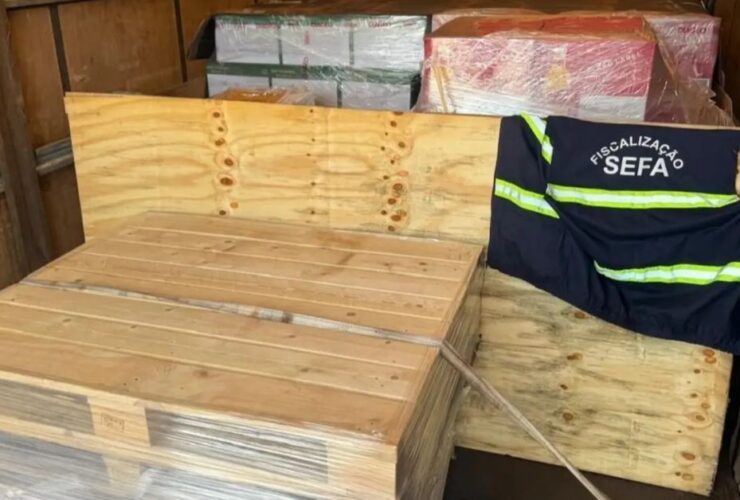 Apresentação da carda de uísque apreendida. As garrafas estão dentro de caixotes de madeiras, por cima deles um colete da Sefa-PA