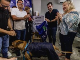 Prefeito Igor Normando tira pano da placa de inauguração do novo hospital veterinário. Na foto, estão outras pessoas e um cachorro