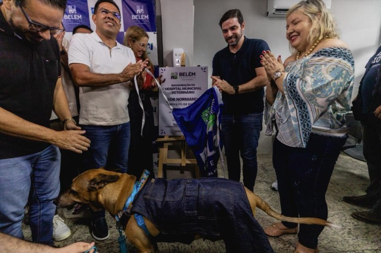 Prefeito Igor Normando tira pano da placa de inauguração do novo hospital veterinário. Na foto, estão outras pessoas e um cachorro