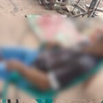 Homem sentado em cadeira, cabeça jogada para trrás. Ele veste bermuda, camisa, boné e chinelo. A foto está embaçada