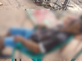 Homem sentado em cadeira, cabeça jogada para trrás. Ele veste bermuda, camisa, boné e chinelo. A foto está embaçada