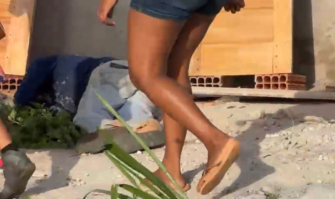 Homem caído ao chão depois de levar tiros. Mulher em pé olhando ele caído