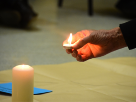 A imagem mostra uma mão pousando uma vela ao lado de outra em simbolismo a uma vigilha