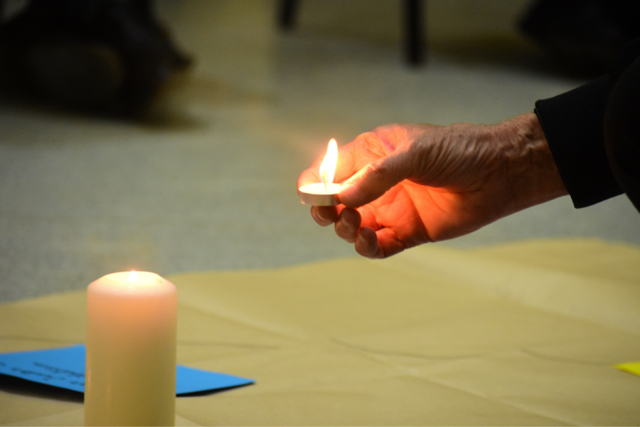 A imagem mostra uma mão pousando uma vela ao lado de outra em simbolismo a uma vigilha