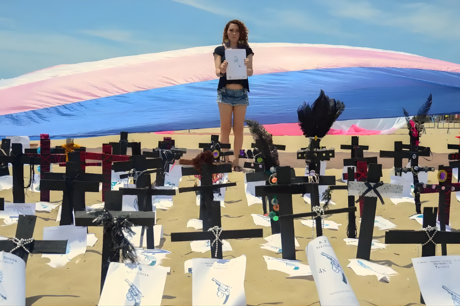 Na praia, cruzes aparencem enterradas na areia em sinal de protesto pela morte de passoas trans