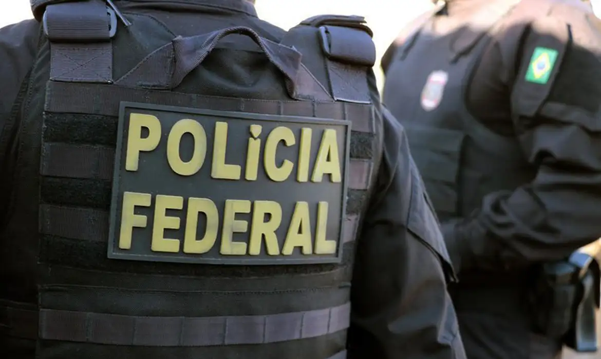 Dois policiais da Polícia Federal usando coletes, em um deles se lê “Polícia Federal”, em imagem em close.