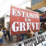 a imagem mostra manifestantes nas ruas com cartazes dizendo que estão em greve