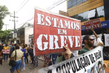 a imagem mostra manifestantes nas ruas com cartazes dizendo que estão em greve