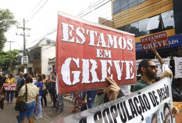 a imagem mostra manifestantes nas ruas com cartazes dizendo que estão em greve