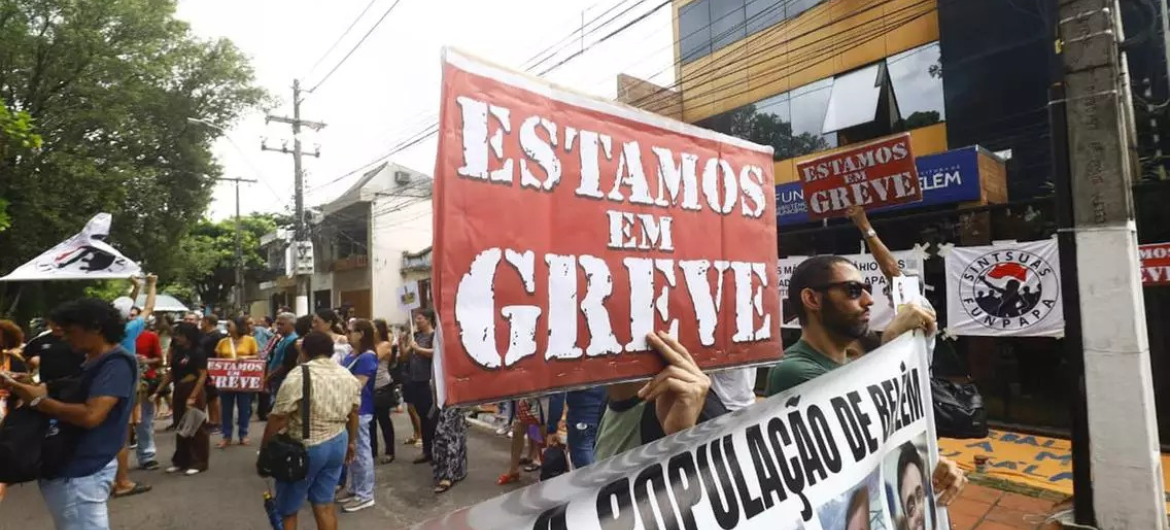 a imagem mostra manifestantes nas ruas com cartazes dizendo que estão em greve