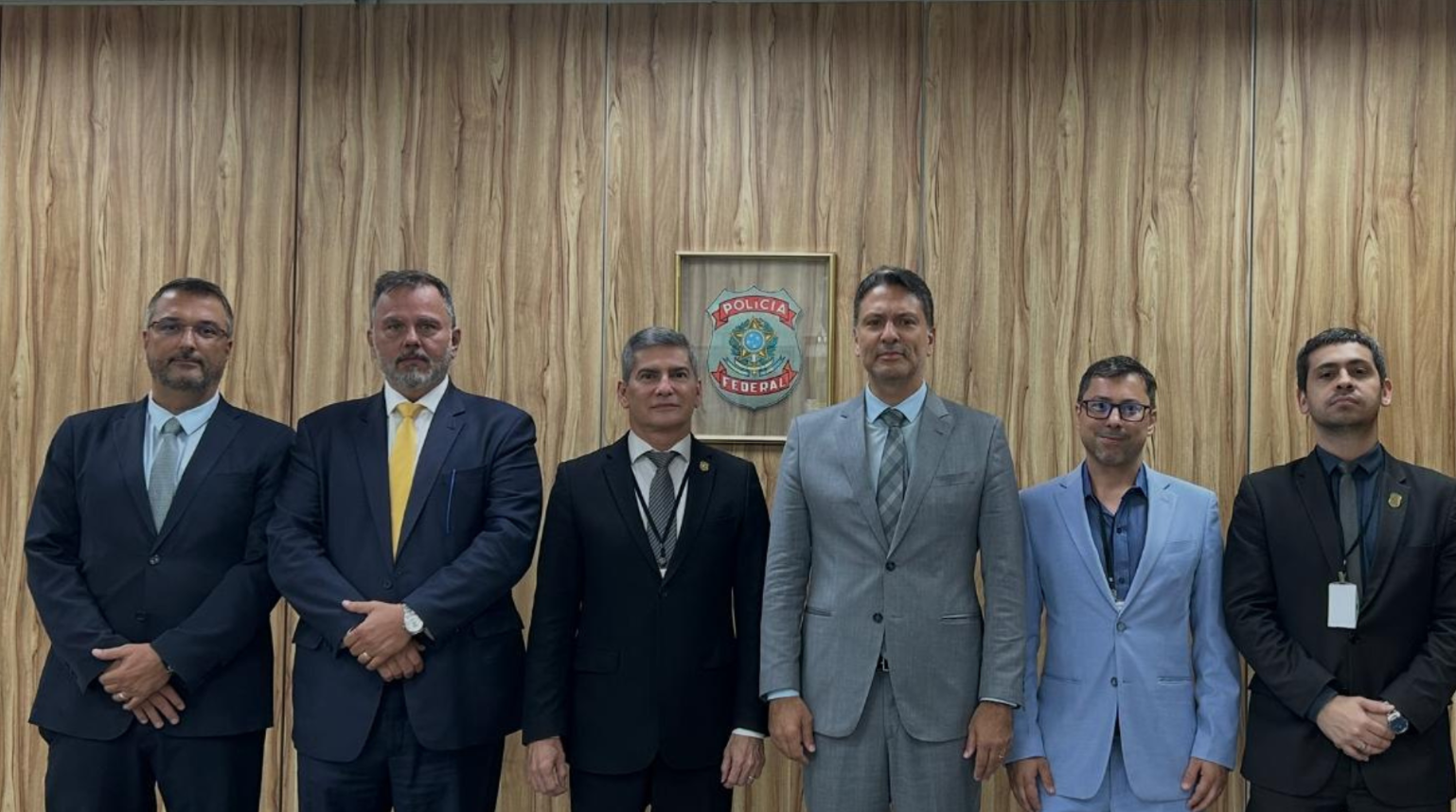 Autoridades da Polícia Civil e da Polícia Federal durante assinatura de acordo de cooperação, reunidas em sala com mesa e bandeiras ao fundo.