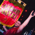 Na imagem um rapaz ergue uma bandeira carnavalesca com o nome da festa "Carnalate!"