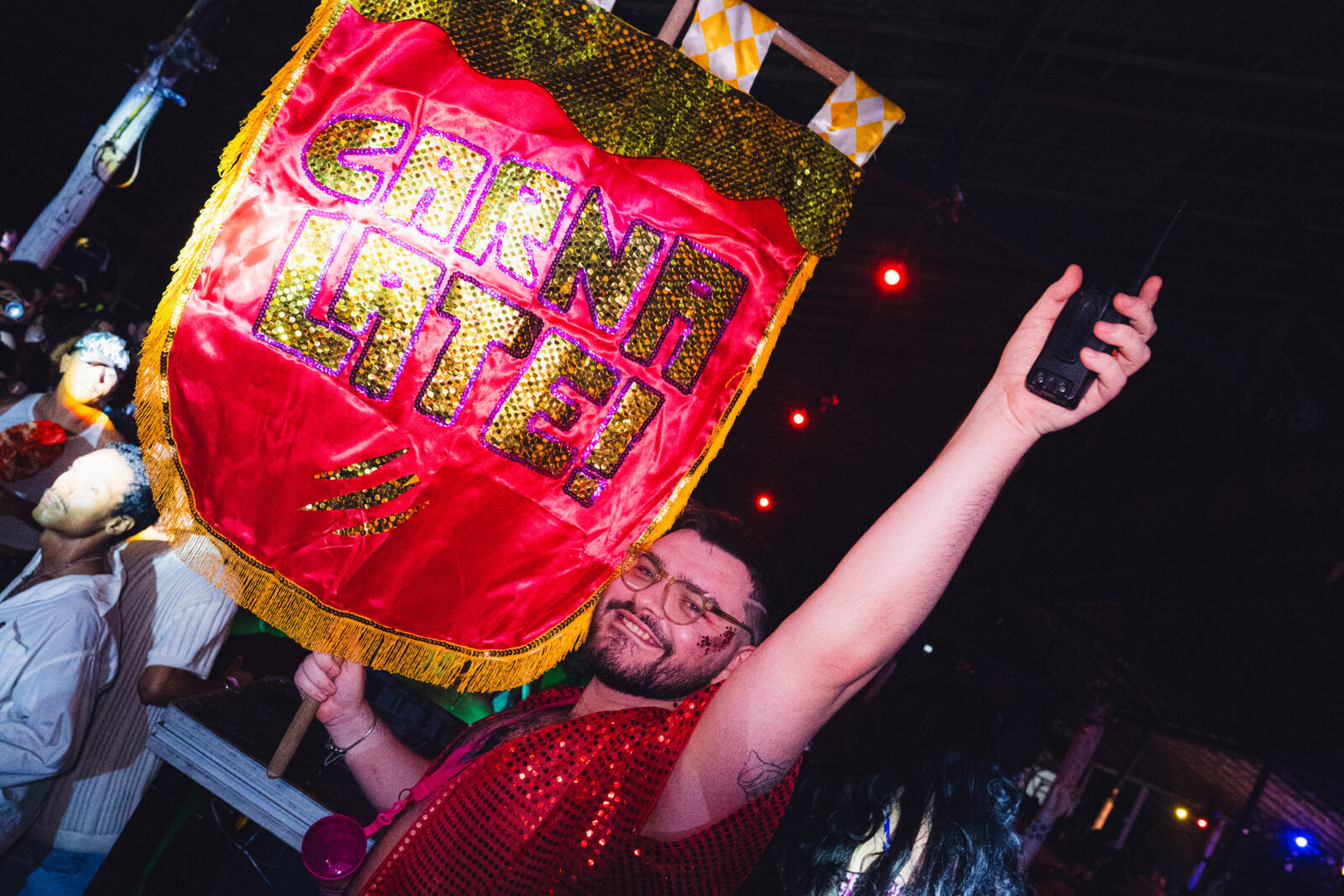 Na imagem um rapaz ergue uma bandeira carnavalesca com o nome da festa "Carnalate!"