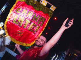 Na imagem um rapaz ergue uma bandeira carnavalesca com o nome da festa "Carnalate!"