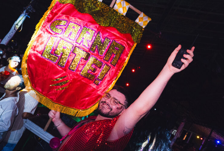 Na imagem um rapaz ergue uma bandeira carnavalesca com o nome da festa "Carnalate!"