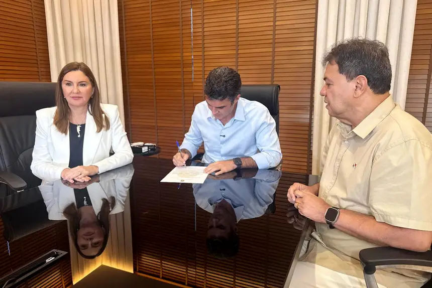 No centro da mesa, o governador Helder Barbalho assina um documento; à direita de Helder, está sentada a vice-governadora Hana Ghassan. À esquerda do governador, está sentado o presidente da ALEPA, o deputado Chicão.