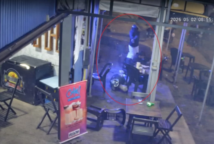 Imagem de câmera de segurança de uma conveniência onde um homem está caído na calçada do estabelecimento enquanto o outro homem que está de pé usando capacete aponta um revólver para ele.