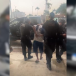 Imagem do suspeito sendo conduzido até a delegacia pelos agentes da polícia civil.